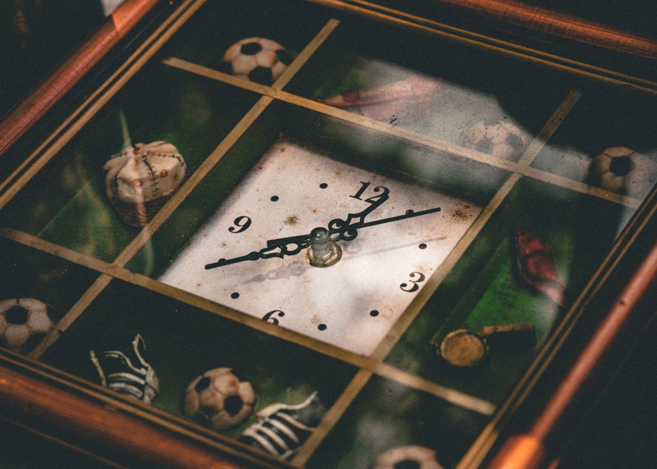 A vintage clock featuring sports-themed decorations like soccer balls and baseballs.