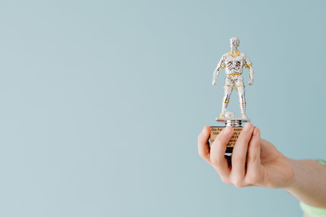 A hand holds a soccer trophy against a blue background, symbolizing success and achievement.